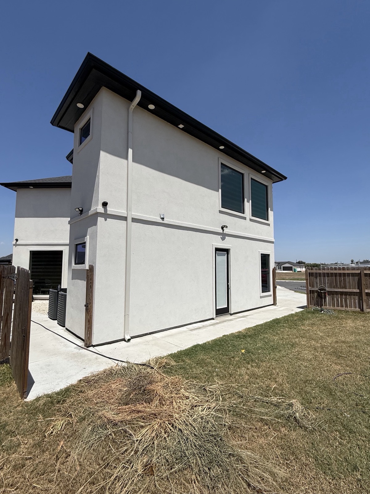 Two-story white stucco home with black seamless gutters and a full-length white downspout installed by Texas Gutters Co